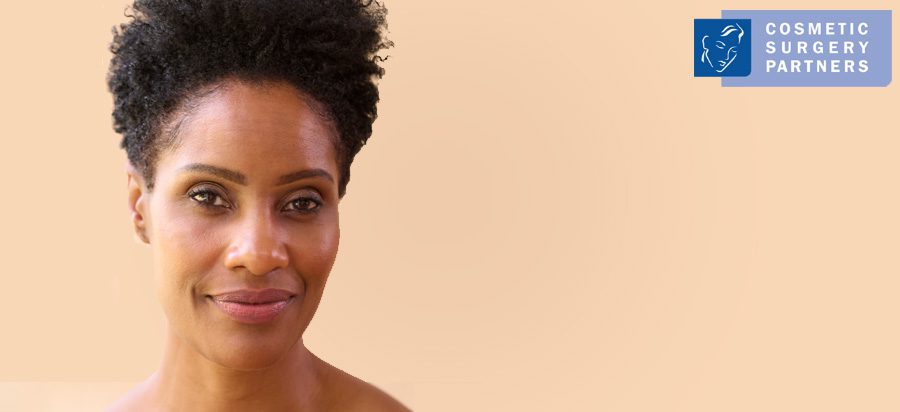 Woman wearing sports bra showing natural breast shape on pink background – Cosmetic Surgery Partners logo in corner.