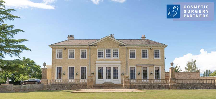 The yellow-brick Grade II listed exterior of Cosmetic Surgery Partners at Hemingford Park Hall, featuring classical architecture and extensive private grounds.